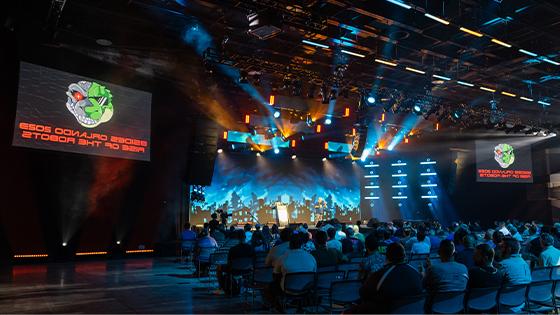 Attendees sit in the Full Sail Live venue. Screens with a lizard robot logo and the words BSides Orlando 2023: Rise of the Robots are on either side of the stage.