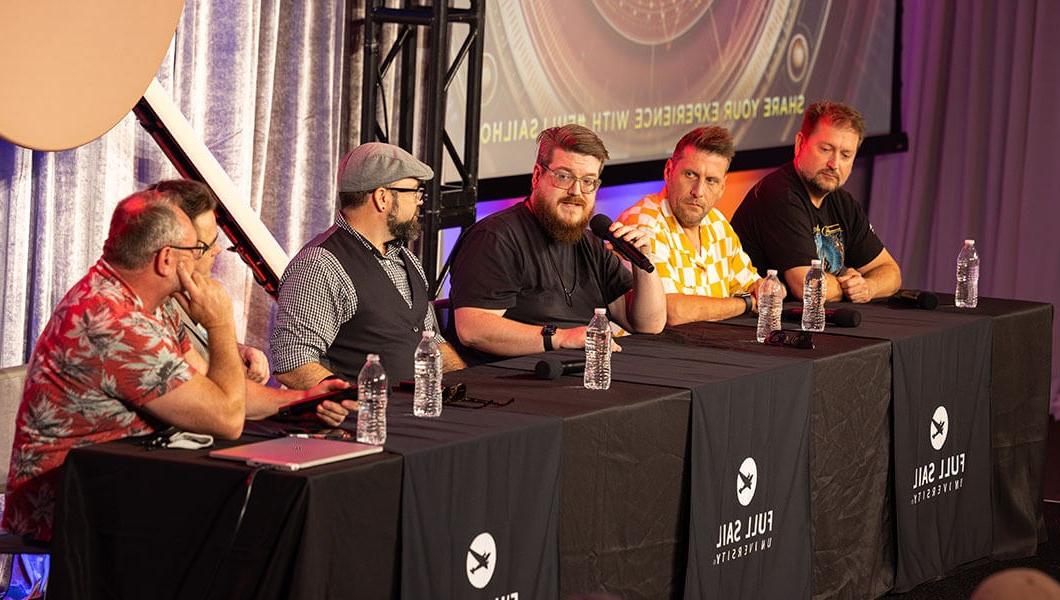 Six men sit at a long table draped in black fabric sheets bearing the 满帆 logo. There is a screen behind them with the words Share Your Experience With #FullSailHOF on it.